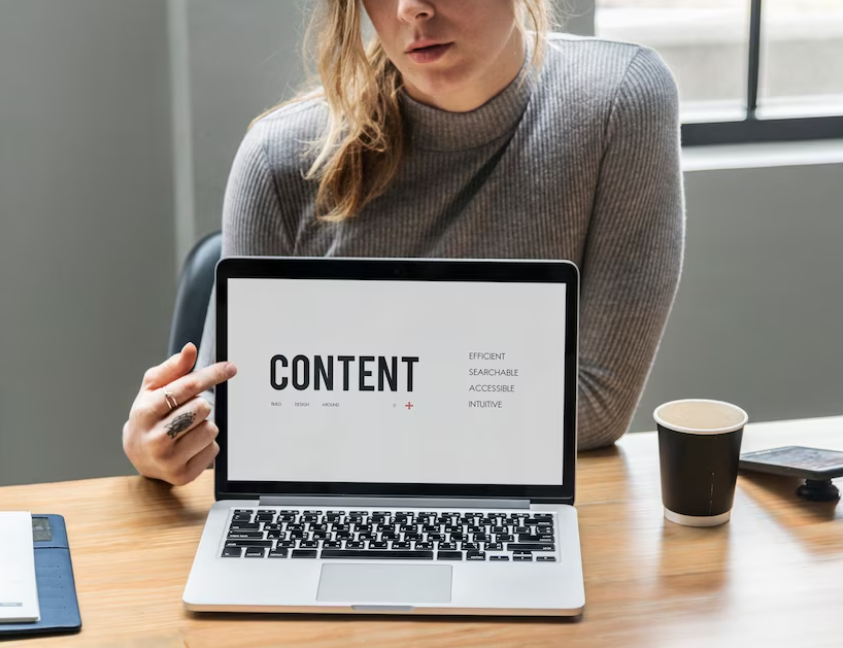 woman sitting at the table and pointing to the opened laptop with word content on it